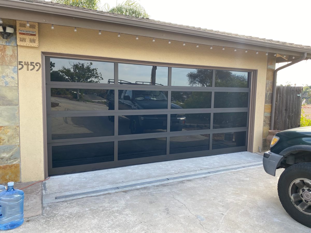 Black full-view glass garage doors during install, our truck on site, San Diego